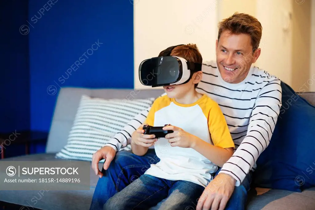 Boy wearing VR glasses playing video game with father on couch at home