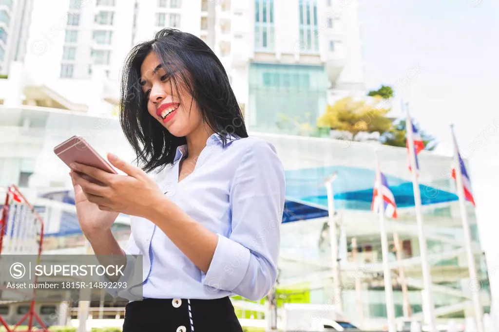 Thailand, Bangkok, smiling businesswoman in the city looking at cell phone