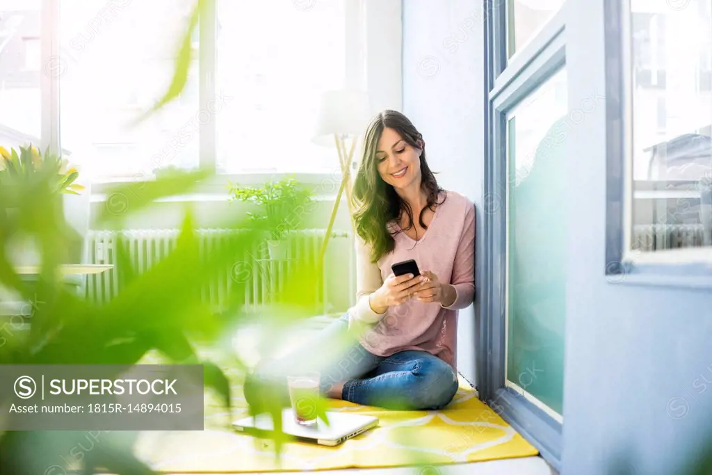 Smiling woman sitting on floor using cell phone