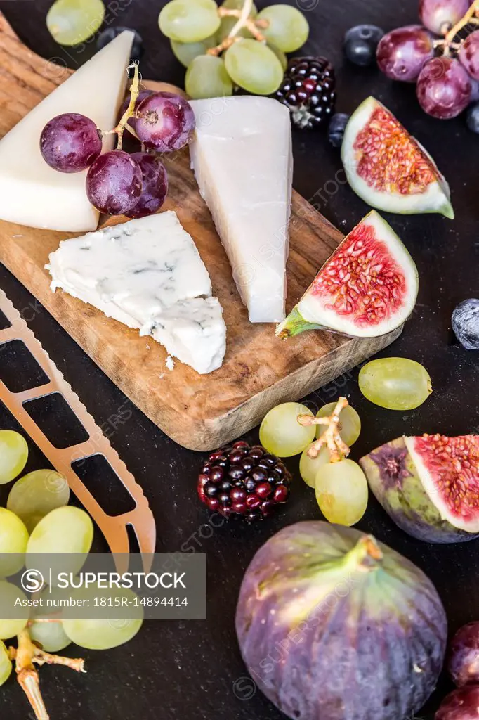 Plate with cheese, figs, grapes, blueberries, brambles, pecan, chopping board, knife