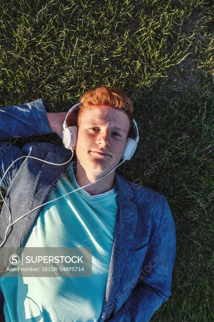Portrait of redheaded young man with headphones lying on grass