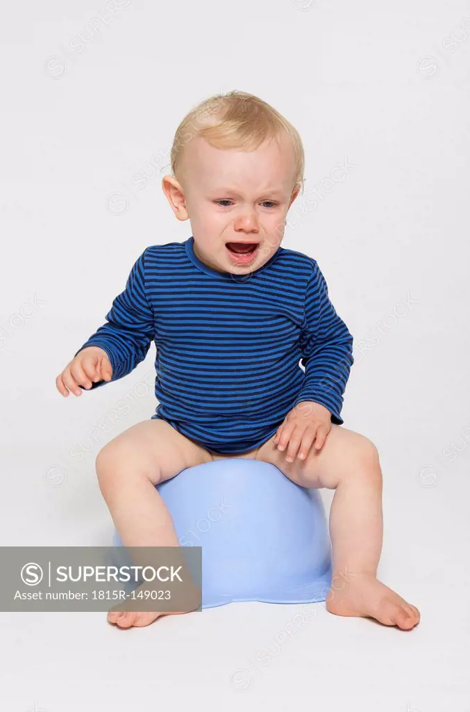 Crying baby boy sitting on his potty, studio shot