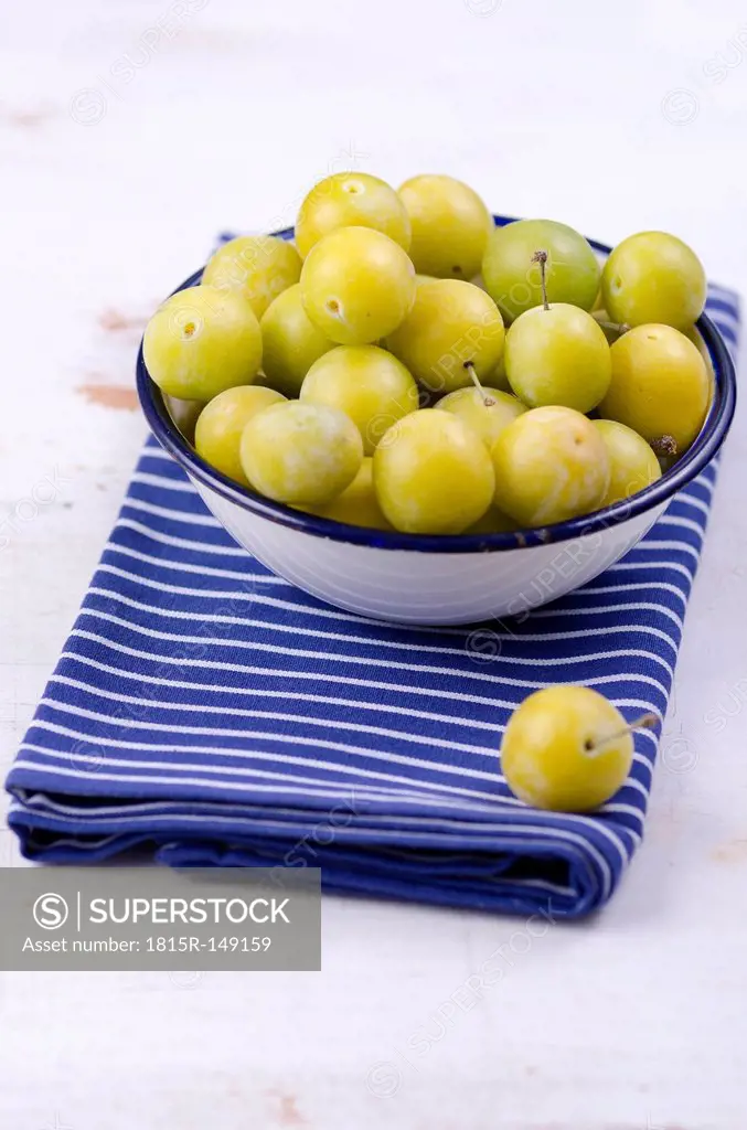 Mirabelles in a bowl and a dish towel on wooden table