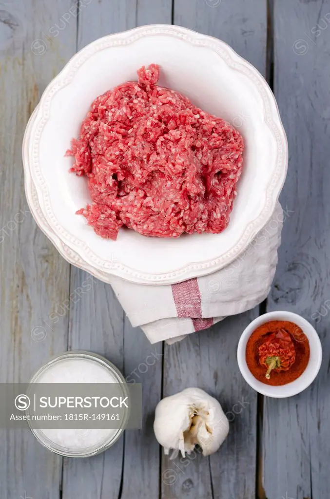Raw ground beef, sea salt, garlic and paprika on wooden table