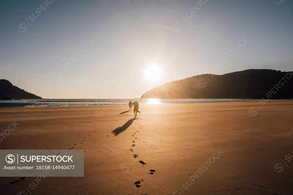Canada, British Columbia, Vancouver Island, two men walking on beach at San Josef Bay at sunset