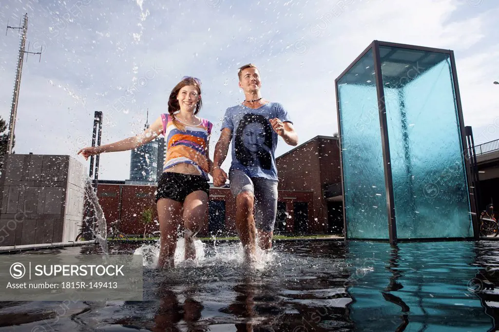 Germany, Bavaria, Munich, Couple running through water at fountain