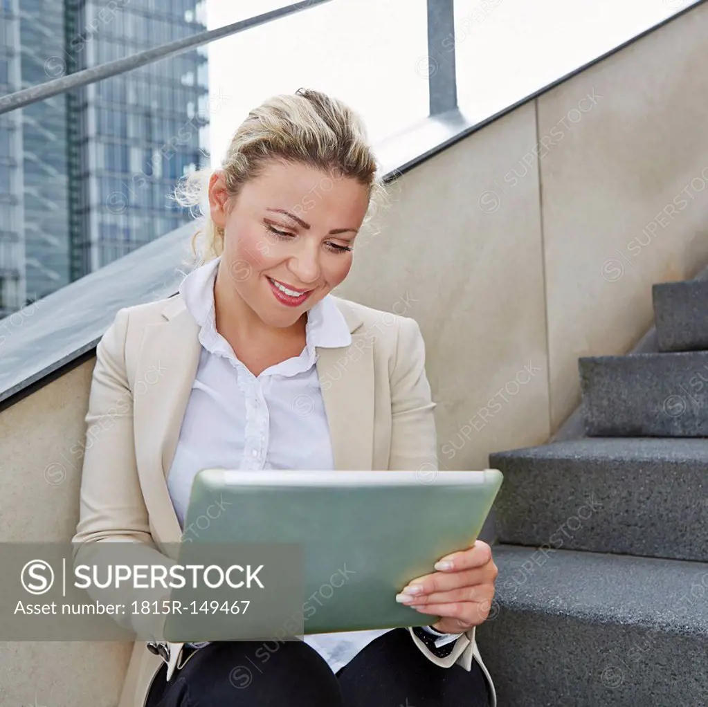 Germany, Cologne, Businesswoman sitting on stairs, using digital tablet