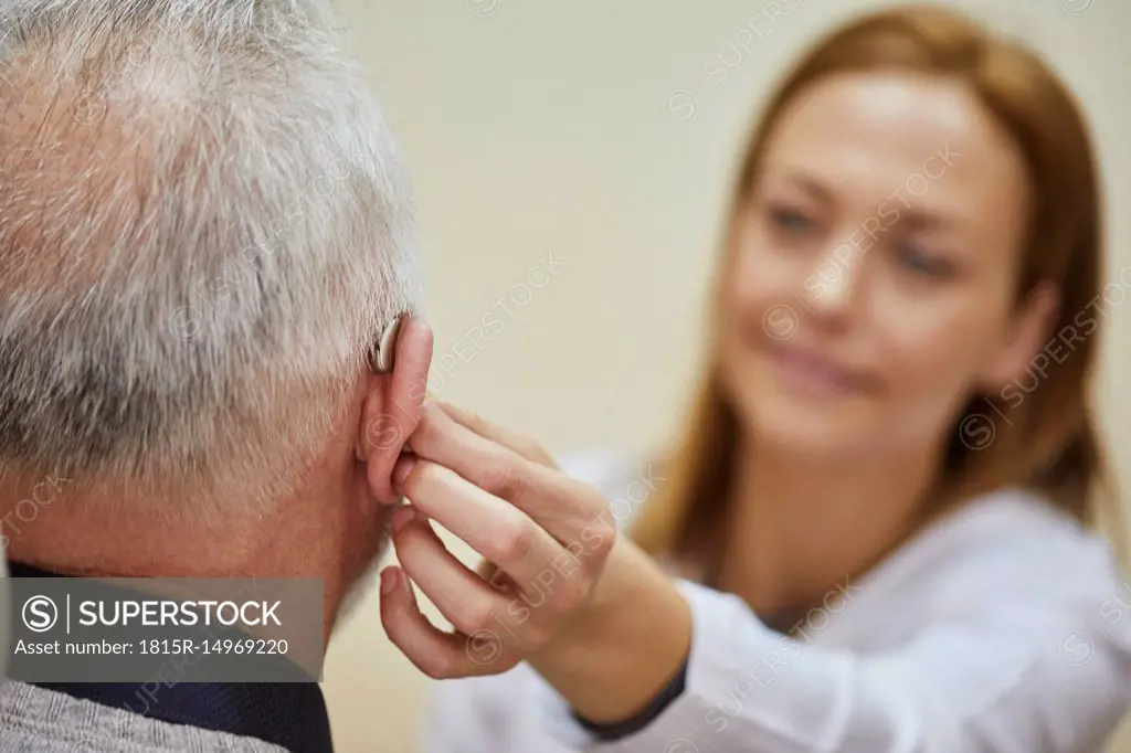 Female doctor applying hearing aid to senior man's ear