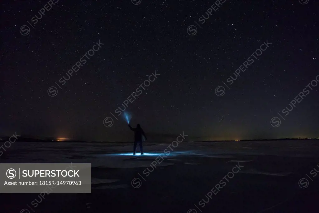 Russia, Amur Oblast, silhouette of man with blue ray standing on frozen Zeya River at night under starry sky