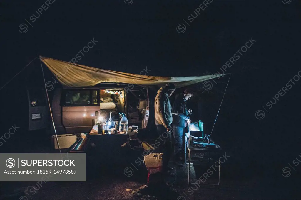 Canada, British Columbia, two men cooking under tarp at minivan at night