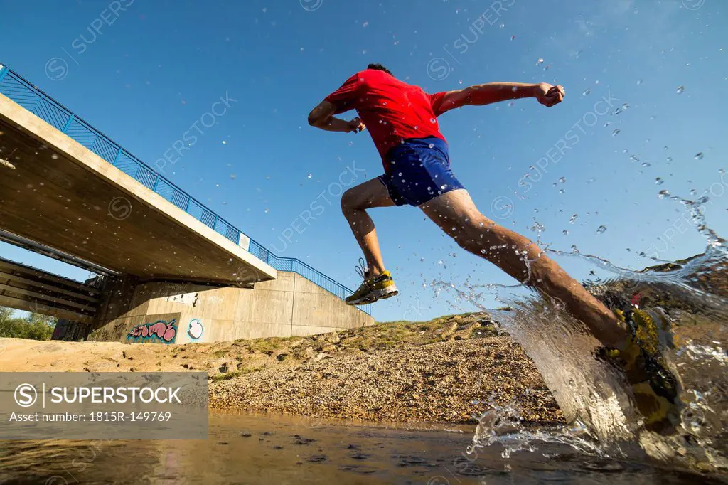 Germany, Baden-Wuerttemberg, Winterbach, athletic young man running through Rems river