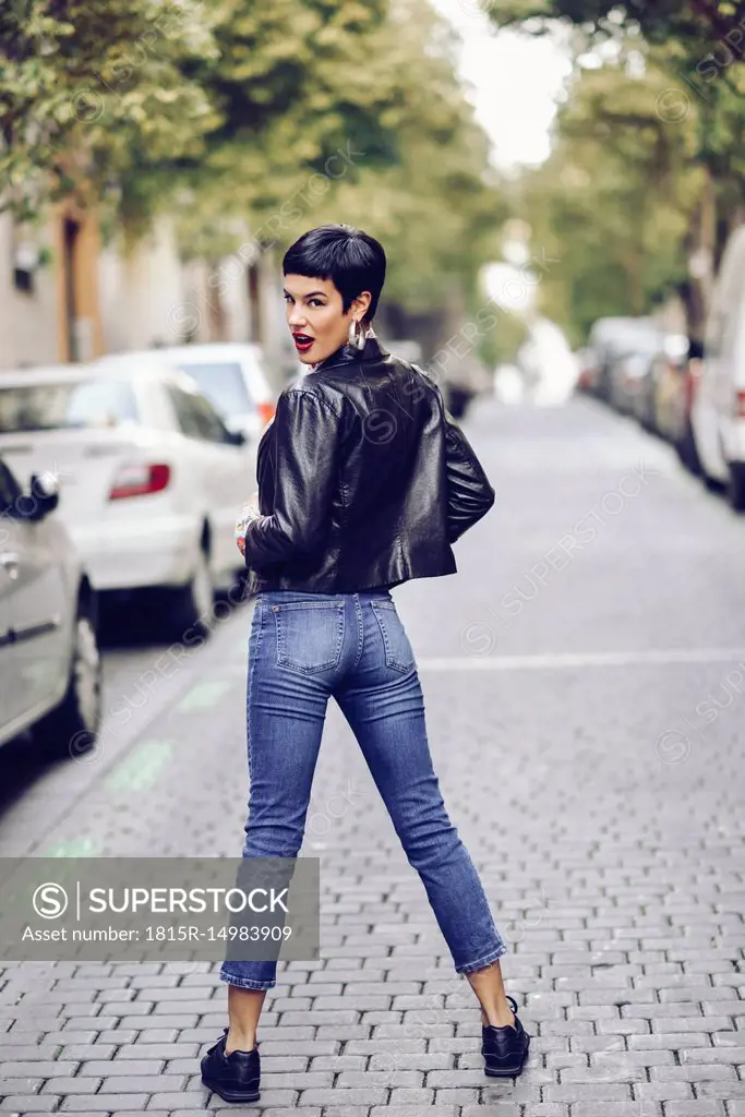 Fashionable young woman wearing jeans and leather jacket standing on street