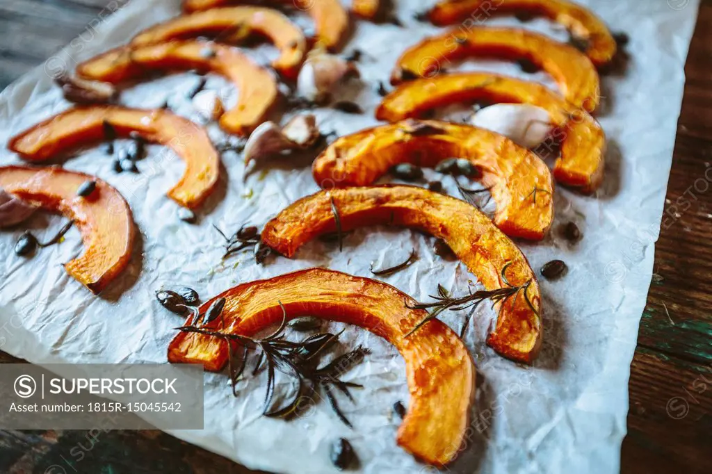 Baked slices of pumpkin, garlic and rosemary on baking paper