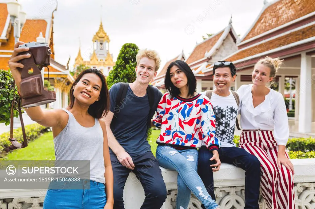 Thailand, Bangkok, five friends taking selfie with smartphone in front of temple complex