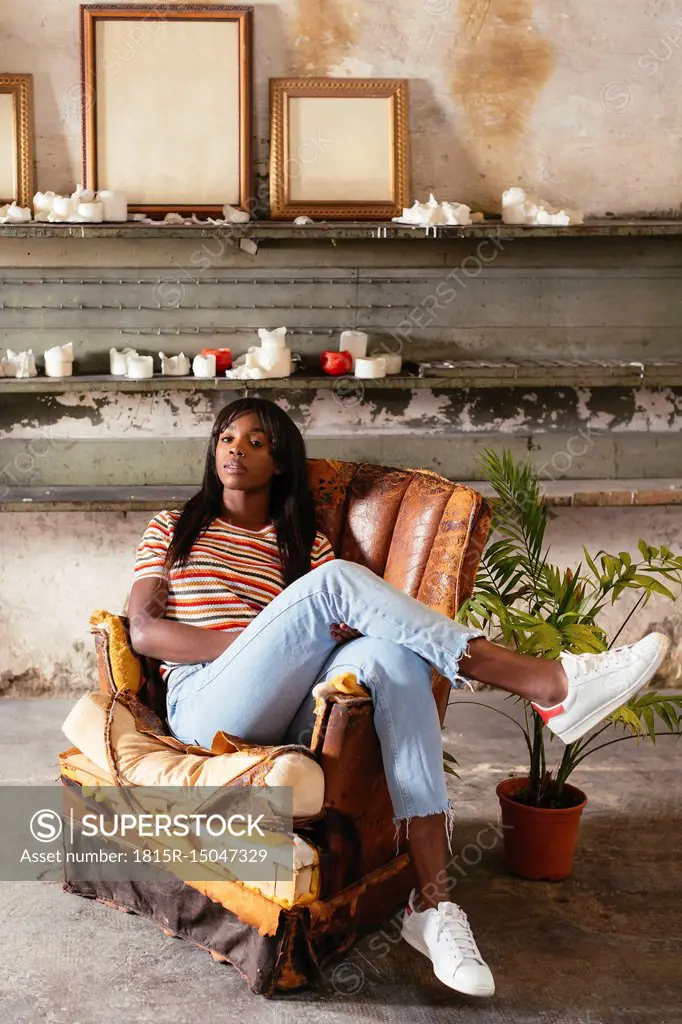 Portrait of cool young woman sitting on an old leather chair in a loft