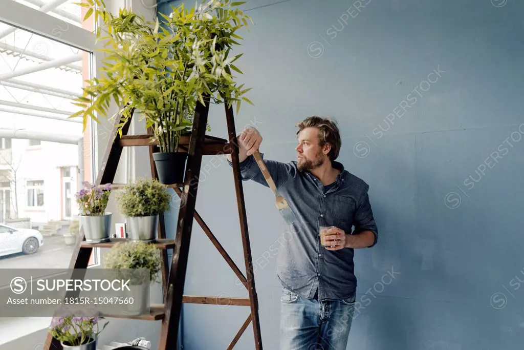 Man with glass of coffee and paint brush looking out of window