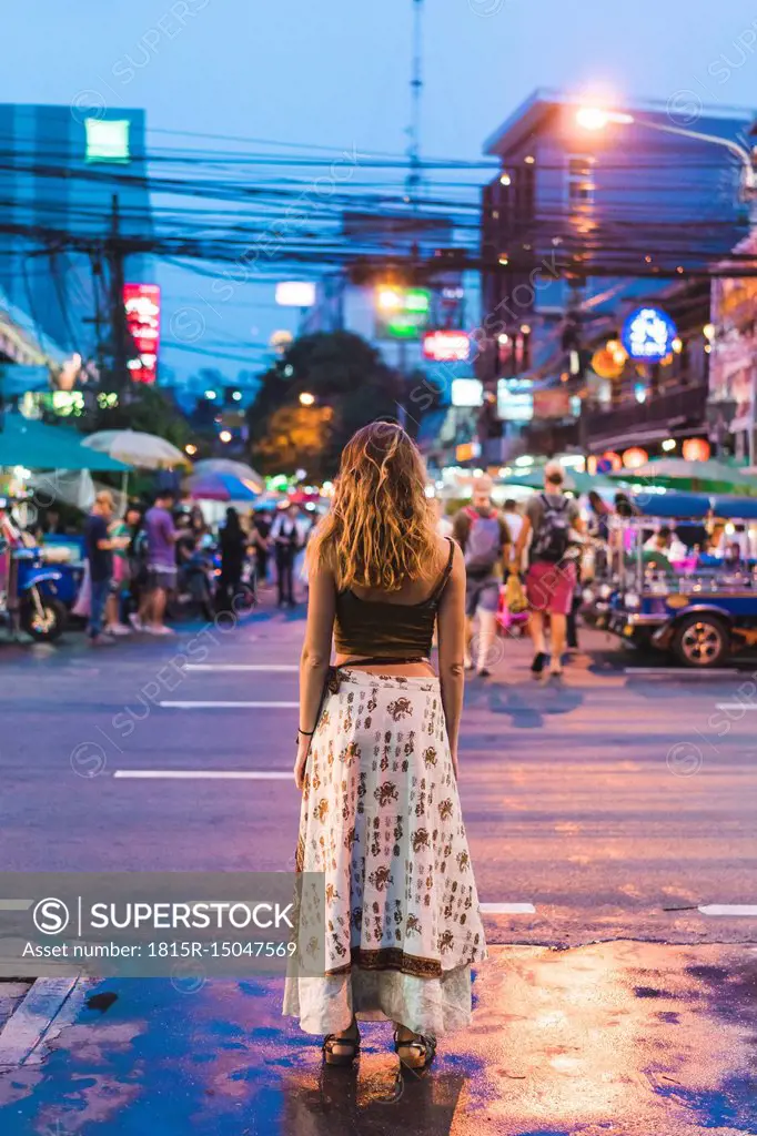Thailand, Bangkok, young woman in the city standing on the street at night