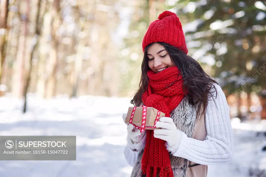 Portrait of happy young woman with Christmas gift in winter forest