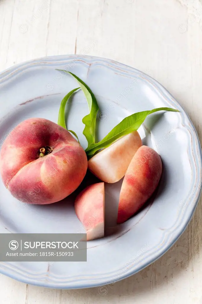 Vineyard peach (Prunus persica) and slices of vineyard peach on plate, studio shot
