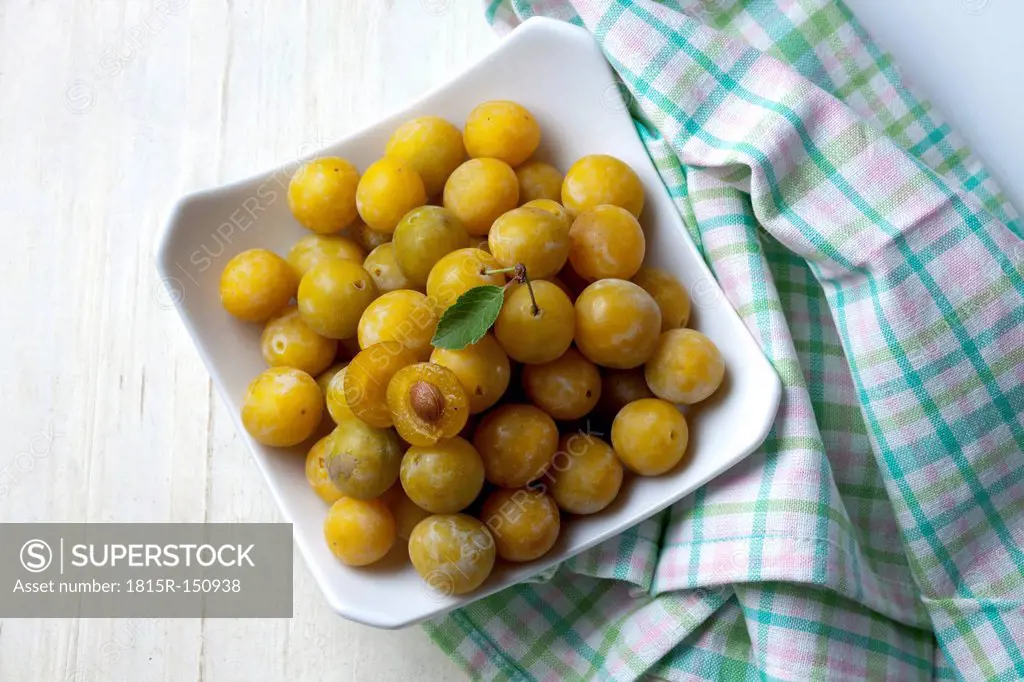 Mirabelles (Prunus domestica subsp. syriaca) in a bowl on wooden table, studio shot