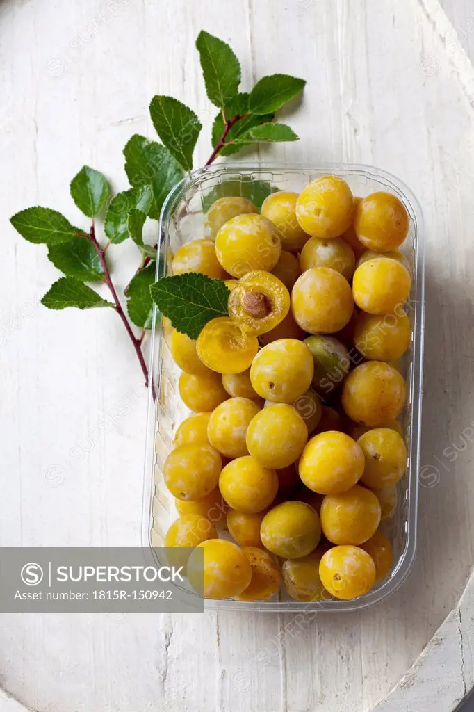 Mirabelles (Prunus domestica subsp. syriaca) in a plastic box on wooden table, studio shot