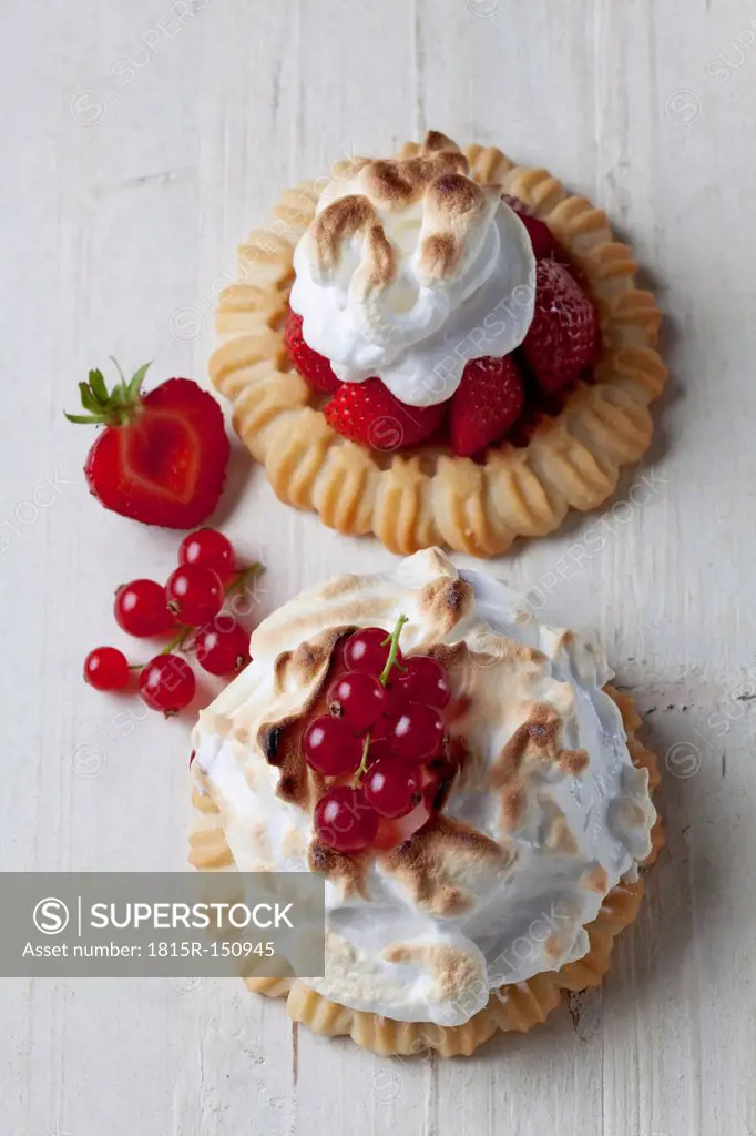 Two meringue tartlets with red currants and strawberries on wood, studio shot