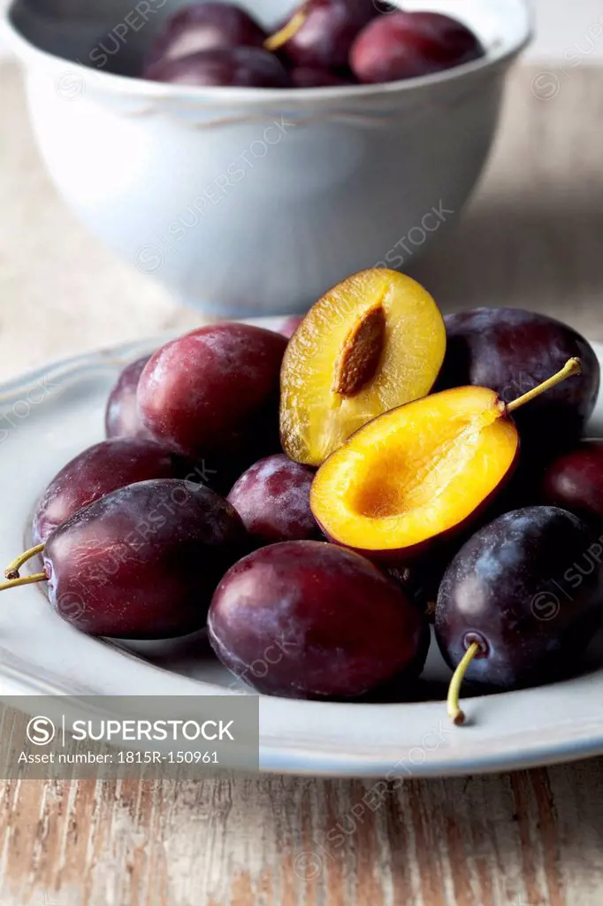 Plate and bowl with plums (Prunus domestica) on wooden table, studio shot