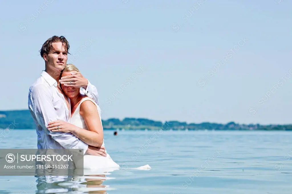 Germany, Bavaria, Tegernsee, Wedding couple standing in lake, man shielding woman's eyes