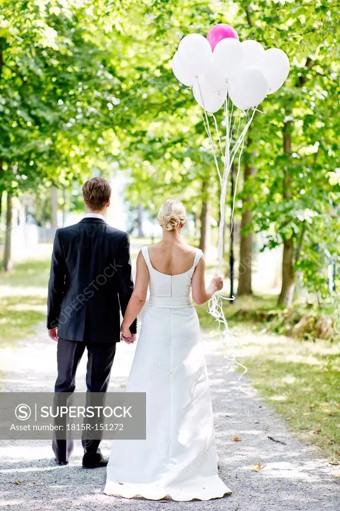Germany, Bavaria, Tegernsee, Wedding couple walking under trees, holding balloons