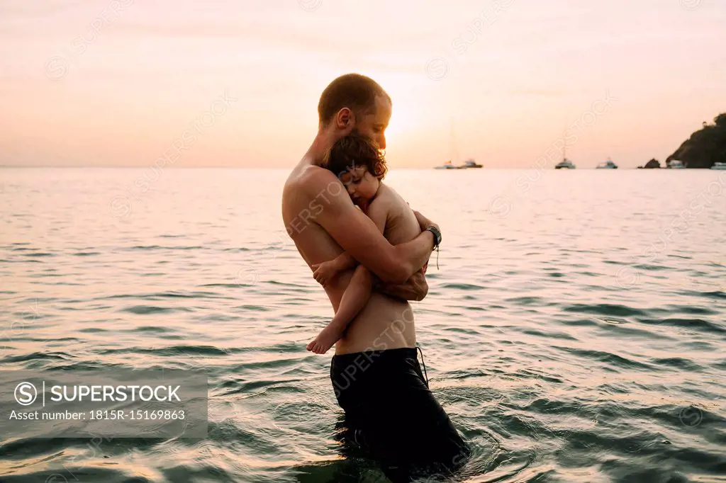 Man carrying little daughter on his arms while wading in the sea