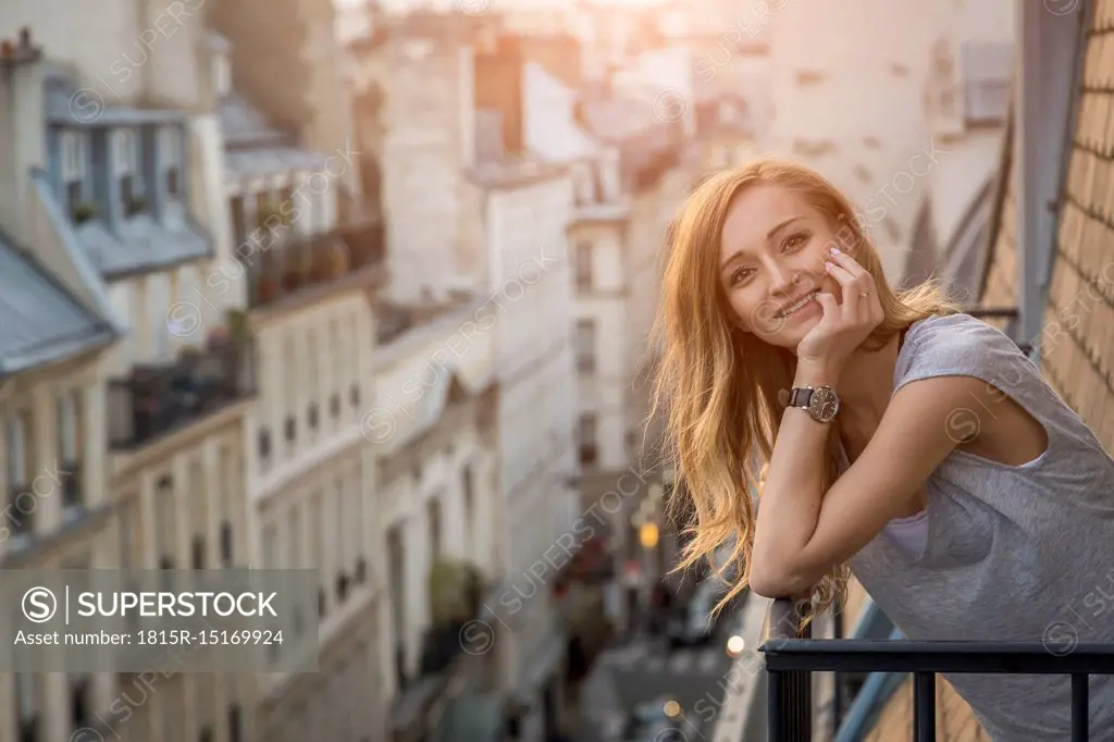 France, Paris, portrait of smiling woman standing on balcony in the evening