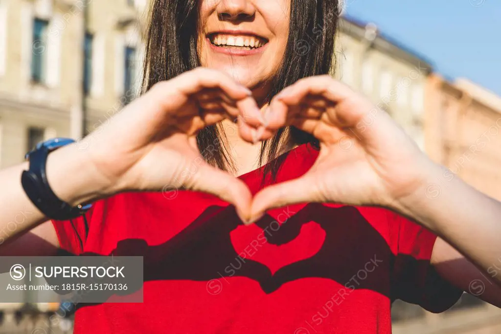 Woman's hands shaping heart, shadow on red t-shirt