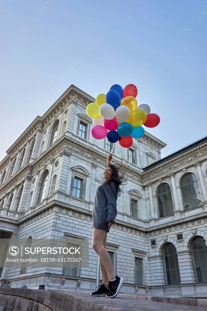 Germany, Munich, happy young woman with bunch of balloons