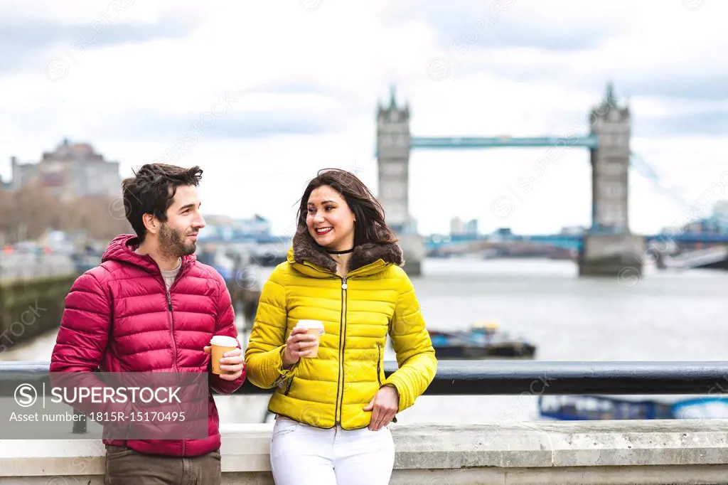 UK, London, couple with coffee to go standing on bridge over the Thames