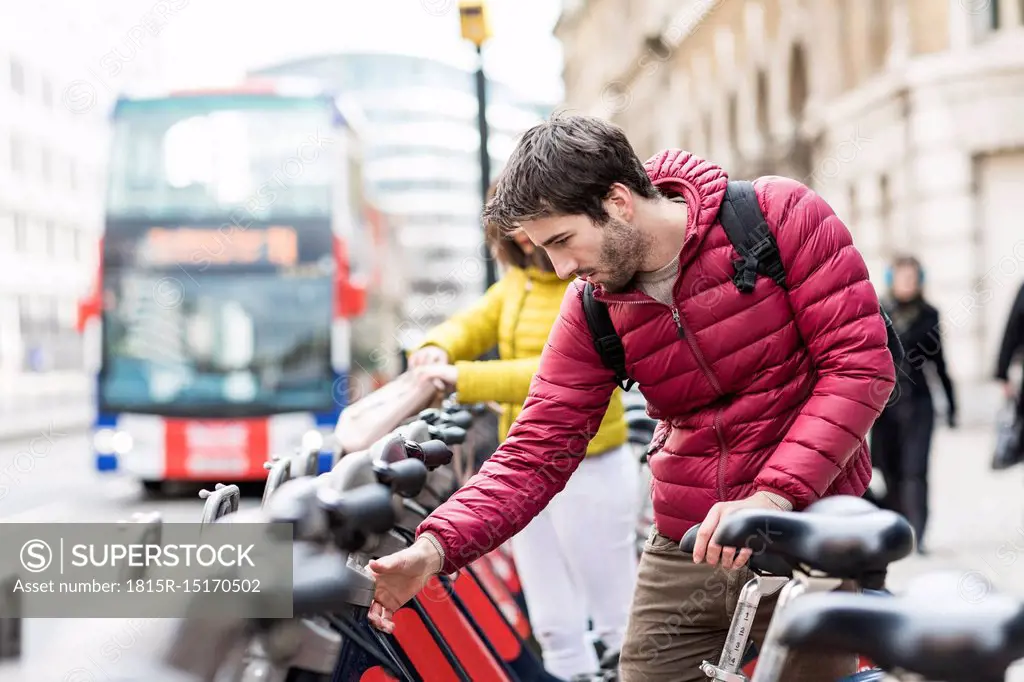 UK, London, young man renting bicycle from bike share stand in city