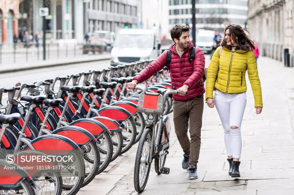 UK, London, young couple with bicycle from bike share stand walking in city