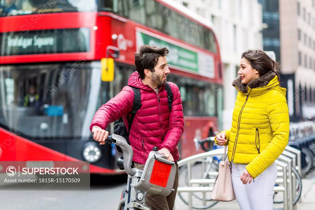 UK, London, young man with rental bicycle from bike share stand talking to his girlfriend