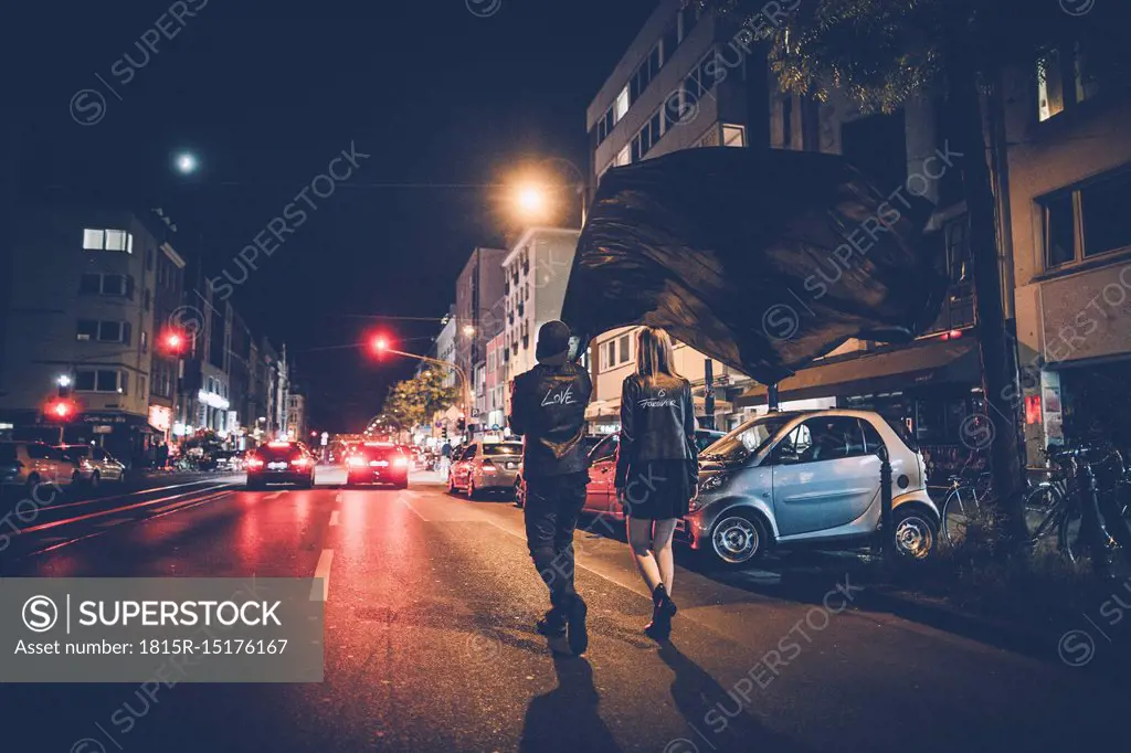 Back view of young couple with black flag walking on the street by night