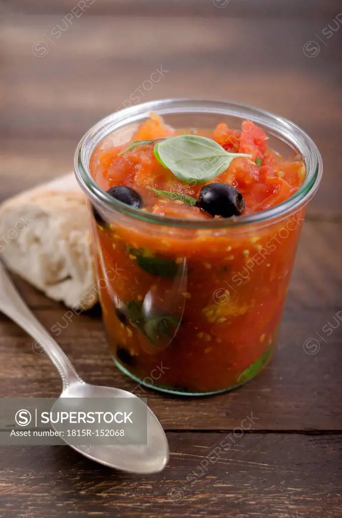 Jelly jar with tomato sauce, black olives and leaves of basil served with white bread, studio shot
