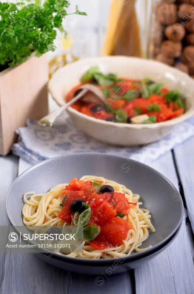 Spaghetti with sauce made of grilled tomatoes with black olives and leaves of basil, studio shot