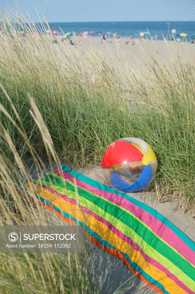 Italy, Adriatic, beach ball and towel on sand dune with grass