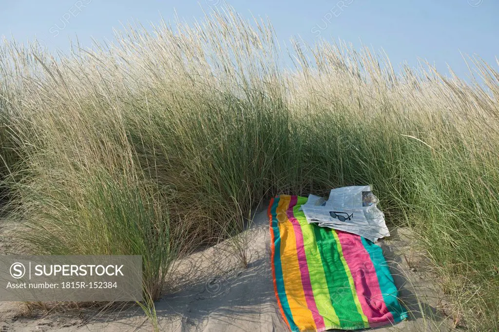 Italy, Adriatic, newspaper, sunglasses and towel on sand dune with grass