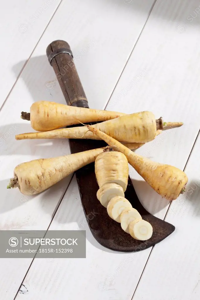 Sliced and whole parsnips (Pastinaca sativa) with antique knife on white wooden table, studio shot