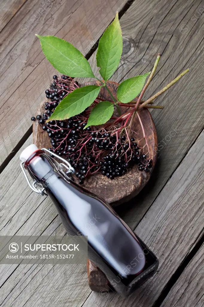 Elderberries (Sambucus), leaves on a wooden shovel and a bottle of elderberry juice on white wooden table, studio shot