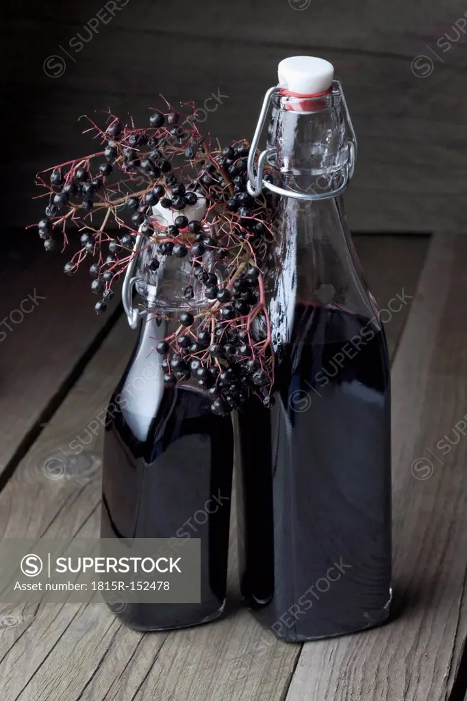 Elderberries (Sambucus) and two bottles of elderberry juice on wooden table, studio shot