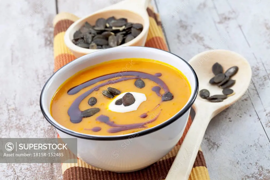 Pumpkin soup in old bowl garnished with pumpkin seed oil, pumpkin seeds and sour cream, studio shot