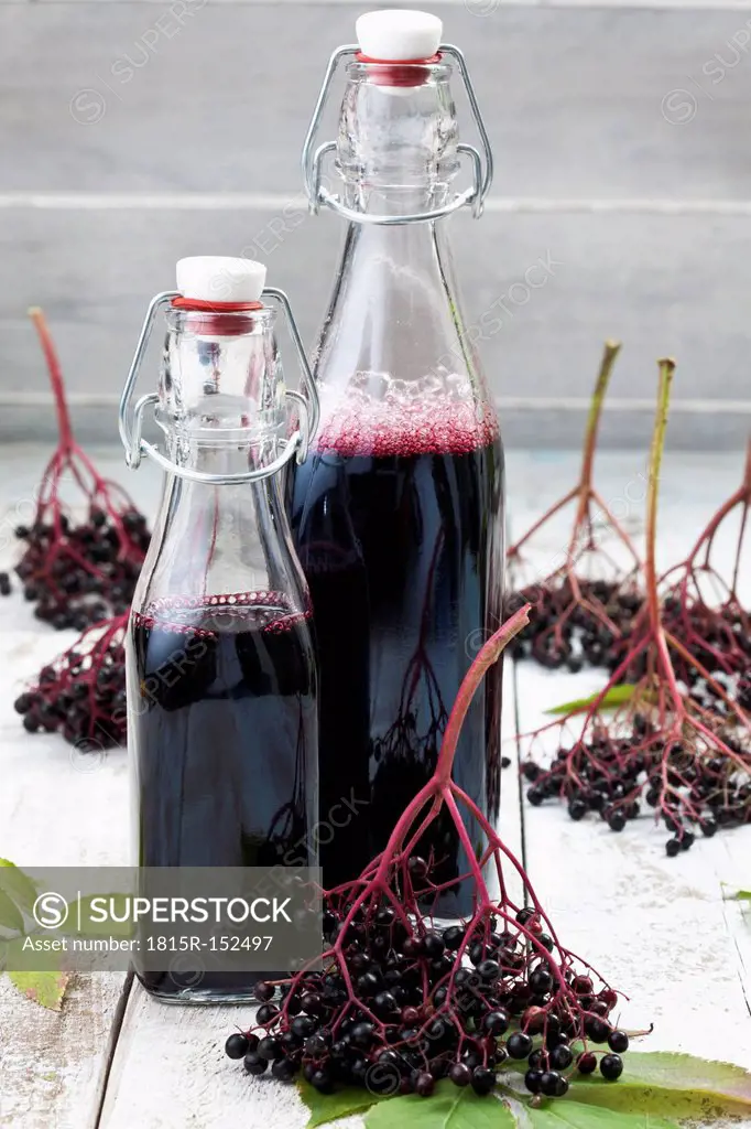 Elderberries (Sambucus) and two bottles of elderberry juice on white wooden table, studio shot