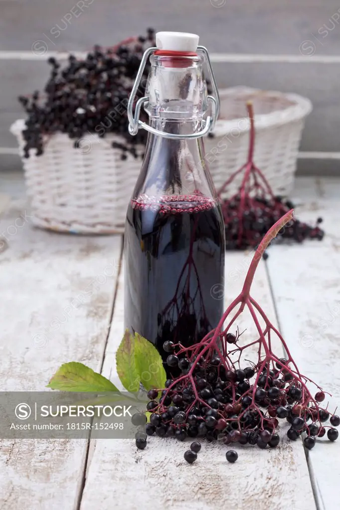Elderberries (Sambucus), basket and a bottle of elderberry juice on white wooden table, studio shot