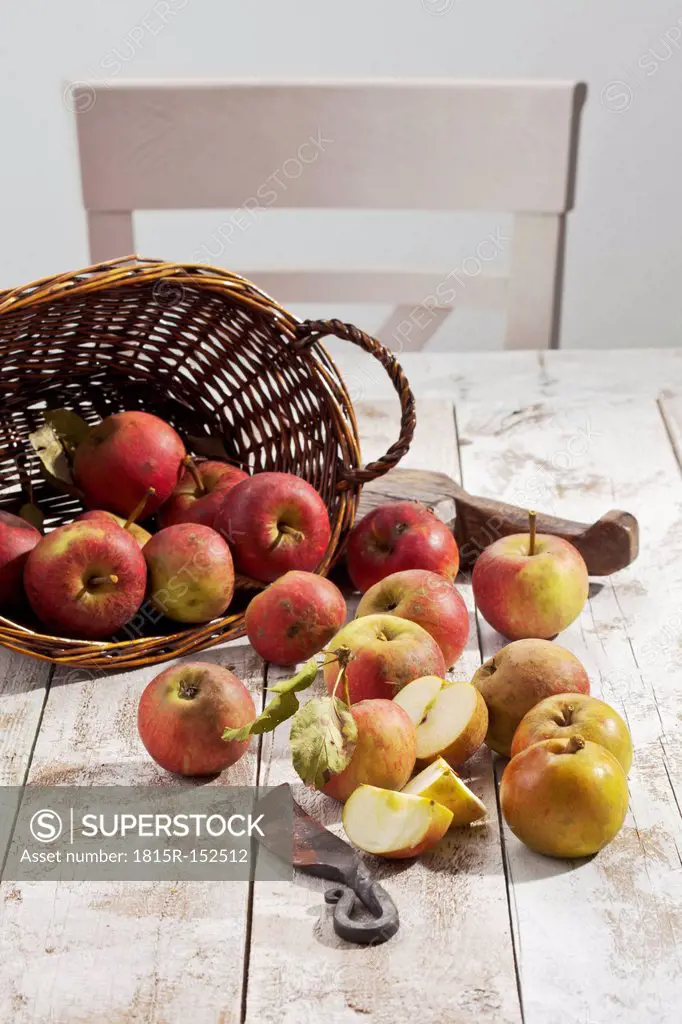 Organic apples (Malus), basket and a knife on white wooden table, studio shot