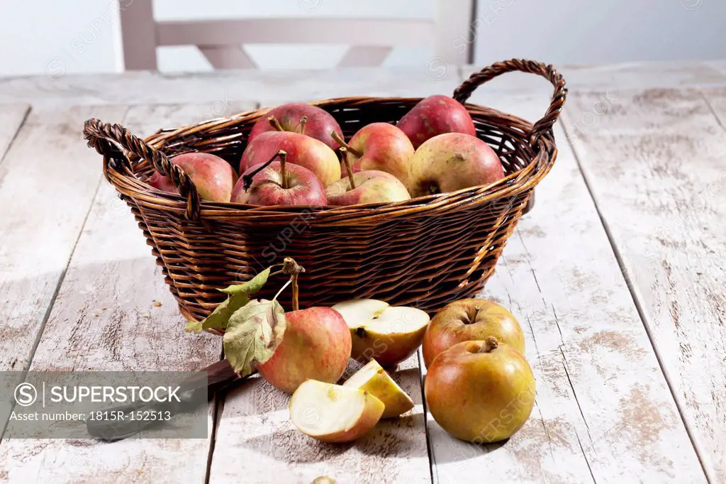 Organic apples (Malus), basket and a knife on white wooden table, studio shot